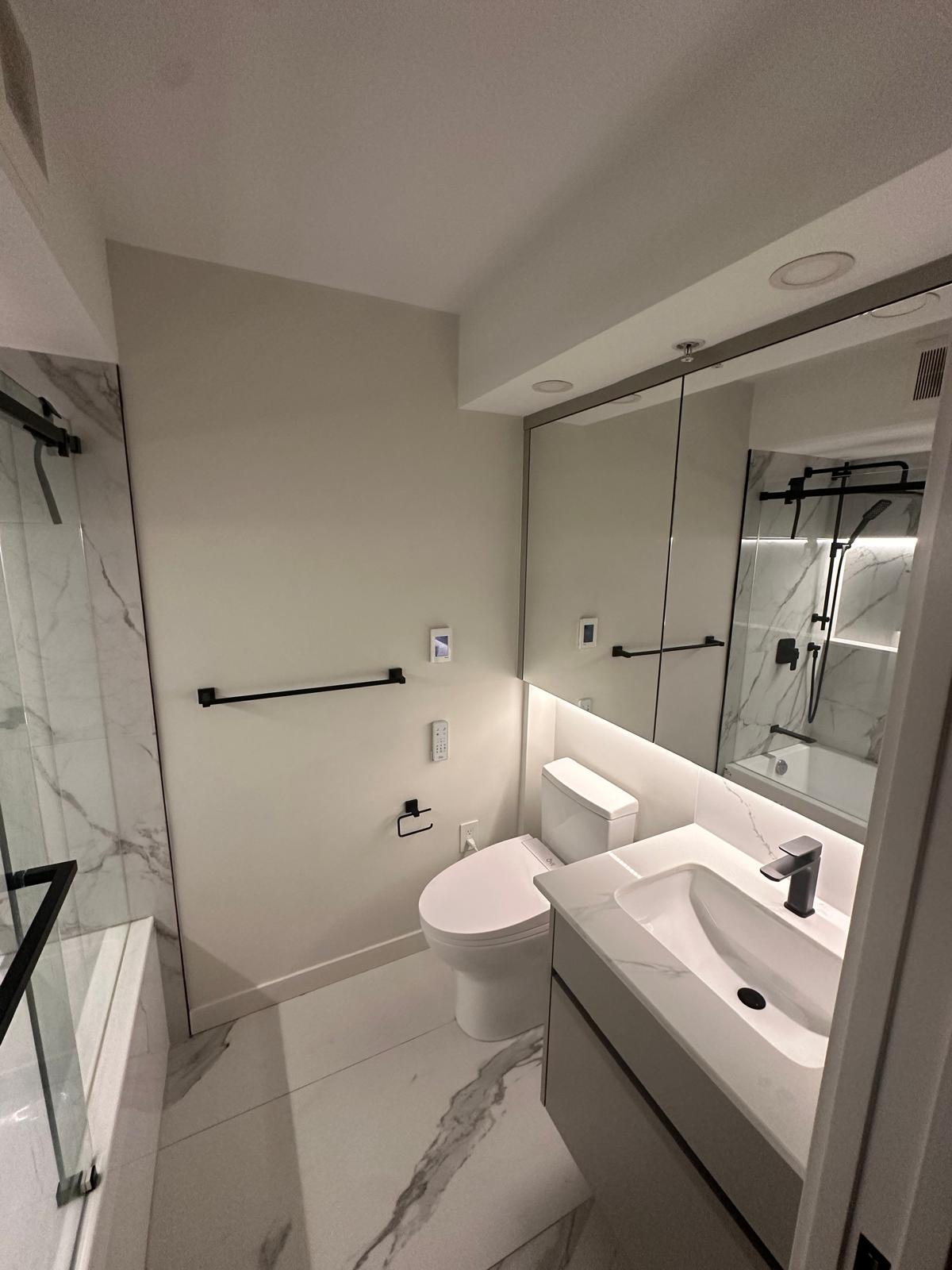 Bathroom finished with marble-look tile, custom vanity, and matte black accents