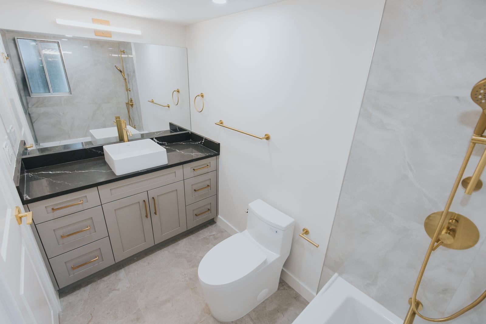 Renovated bathroom with custom vanity, black quartz counter, brushed gold fixtures, and walk-in shower